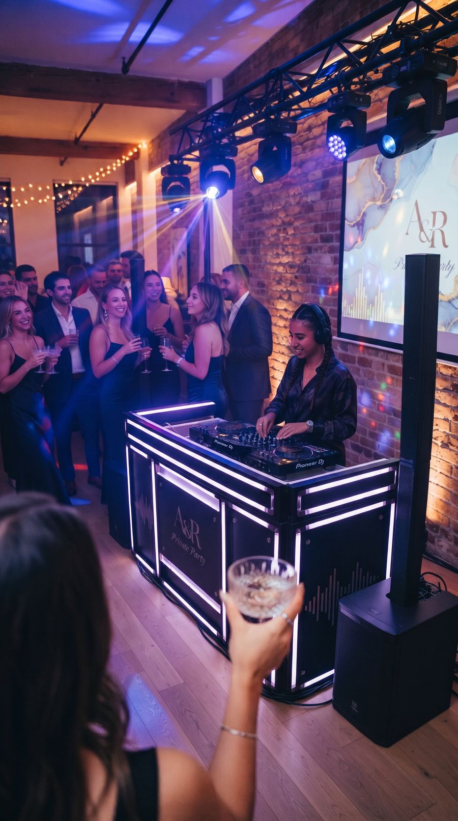 DJ performing at an indoor private party with guests dancing under coloured lighting