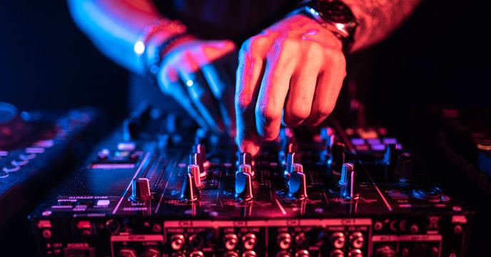 DJ adjusting a live mixing console with red and blue lighting