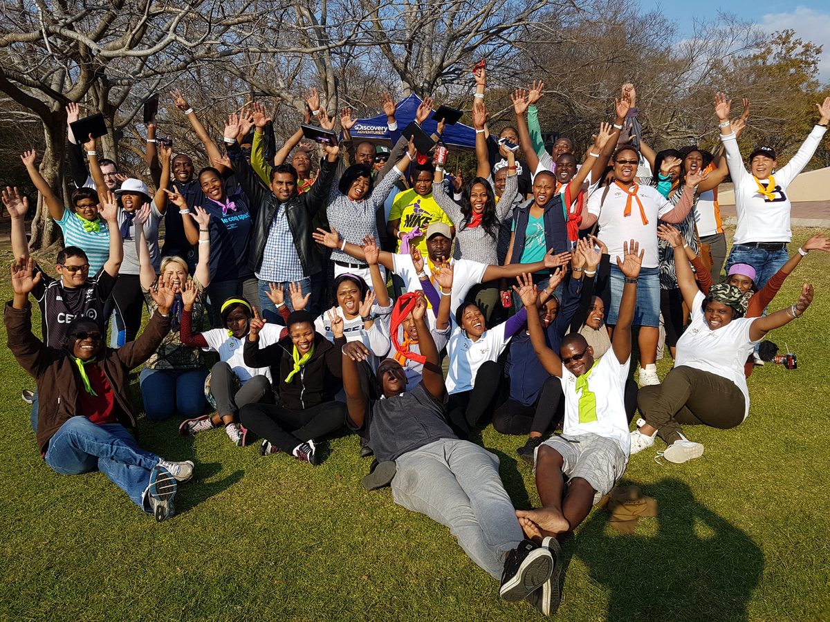Large corporate team cheering with arms raised after an outdoor team building day